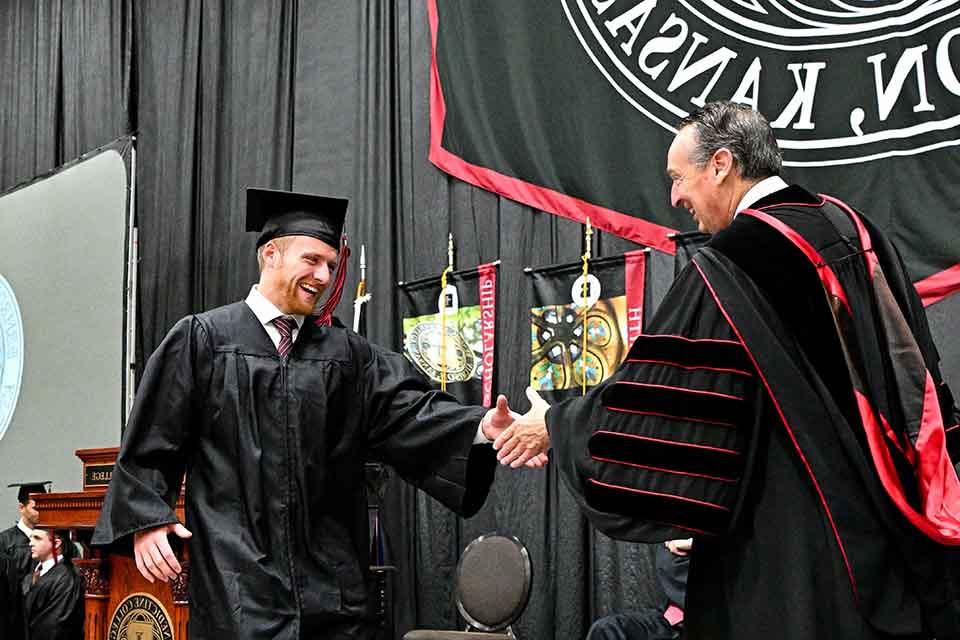 毕业典礼上，一名学生与明尼斯校长握手